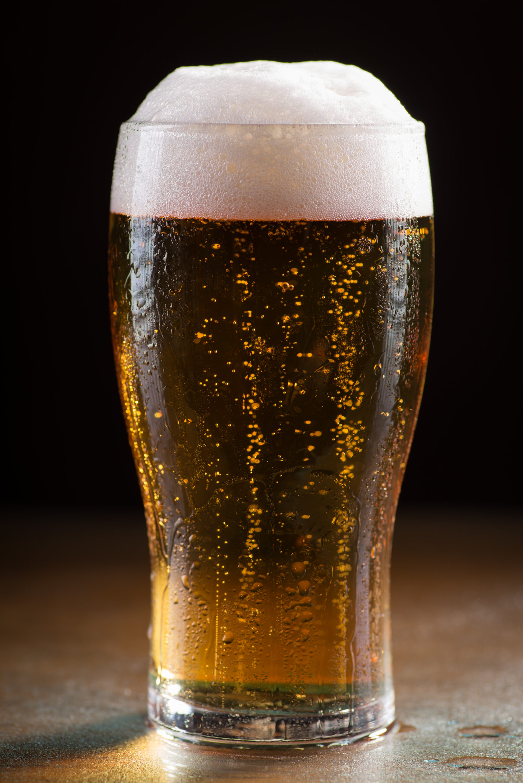 A vertical shot of a glass of cold refreshing beer with foam on a wooden table